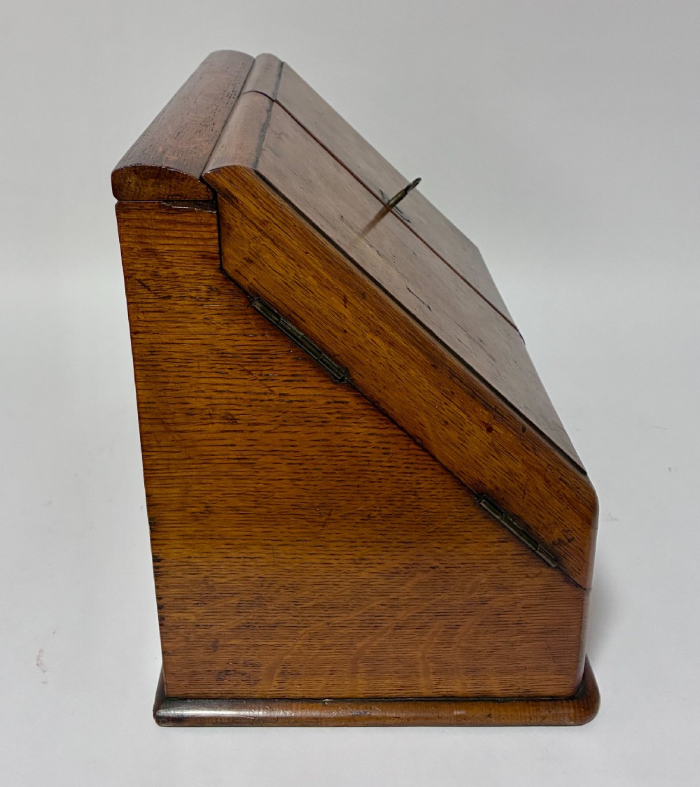 A Victorian oak stationery cabinet featuring sloped double doors, a metal escutcheon with a key, and a moulded plinth base. View XI