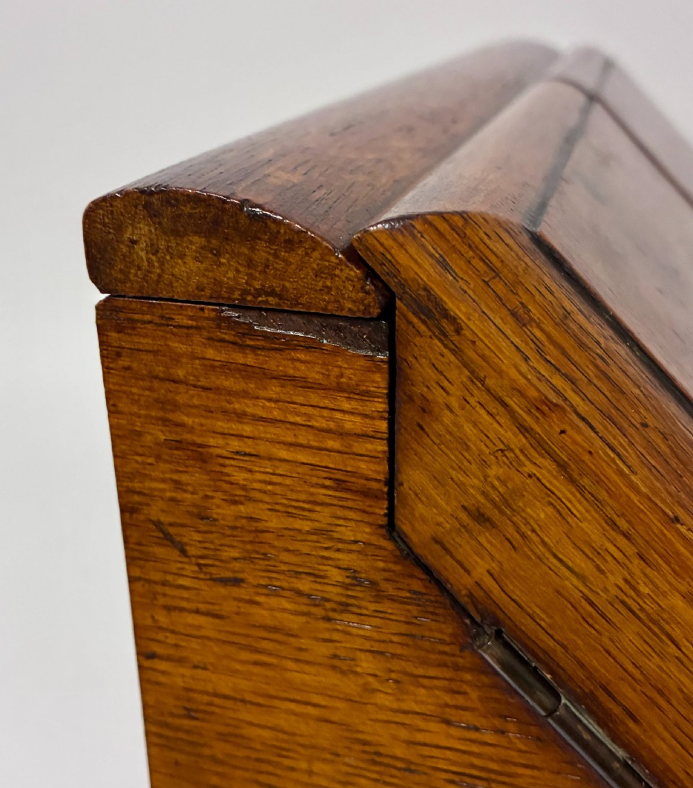 A Victorian oak stationery cabinet featuring sloped double doors, a metal escutcheon with a key, and a moulded plinth base. View XII