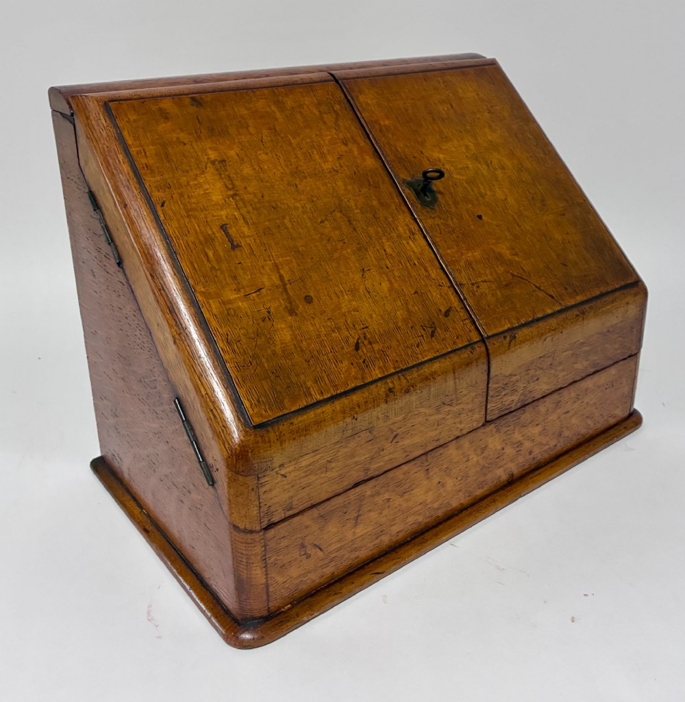 A Victorian oak stationery cabinet featuring sloped double doors, a metal escutcheon with a key, and a moulded plinth base. View XIII