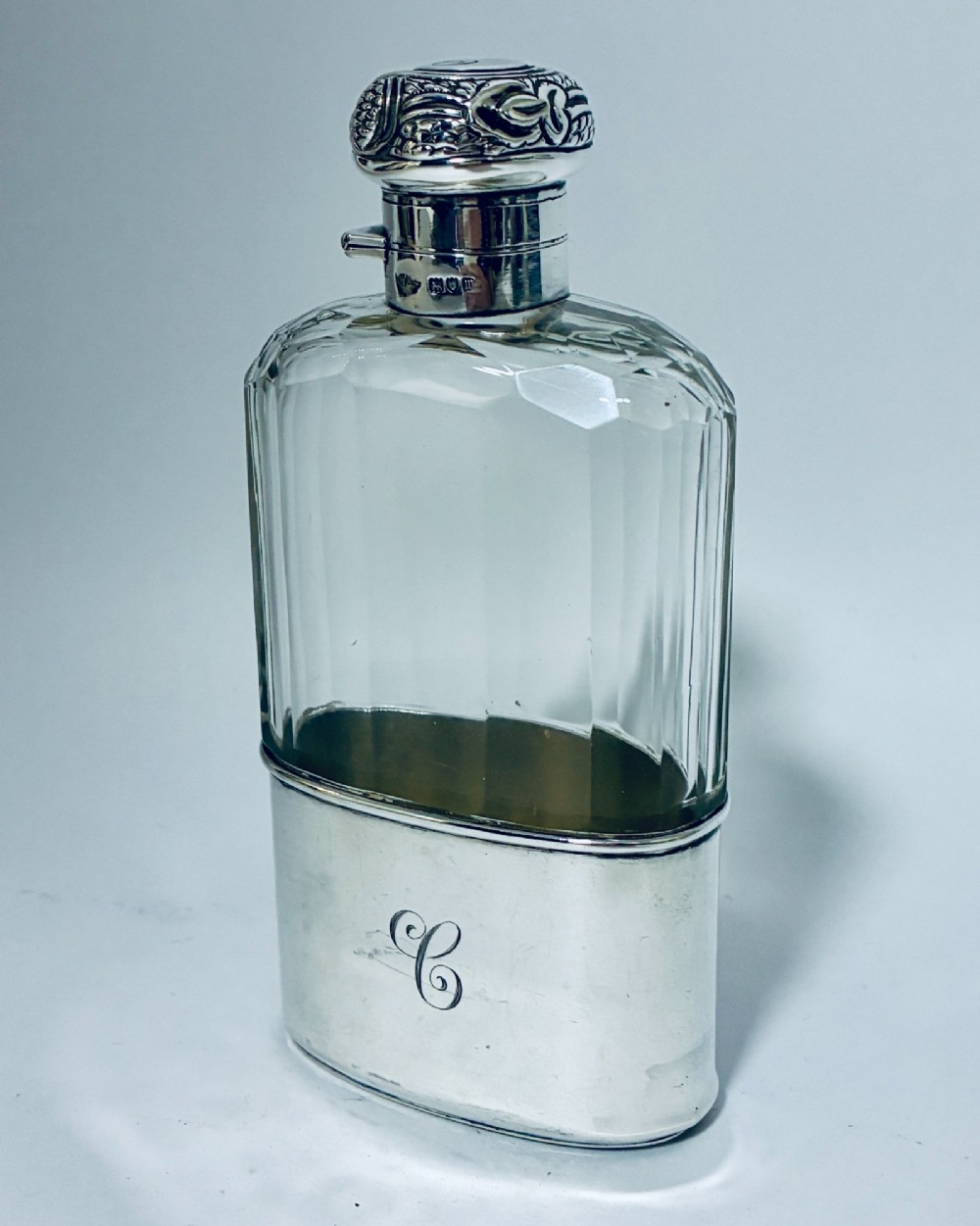 An antique cut-glass hip flask featuring a hallmarked sterling silver collar, chased cap, and a removable silver base cup engraved with the letter C. View II