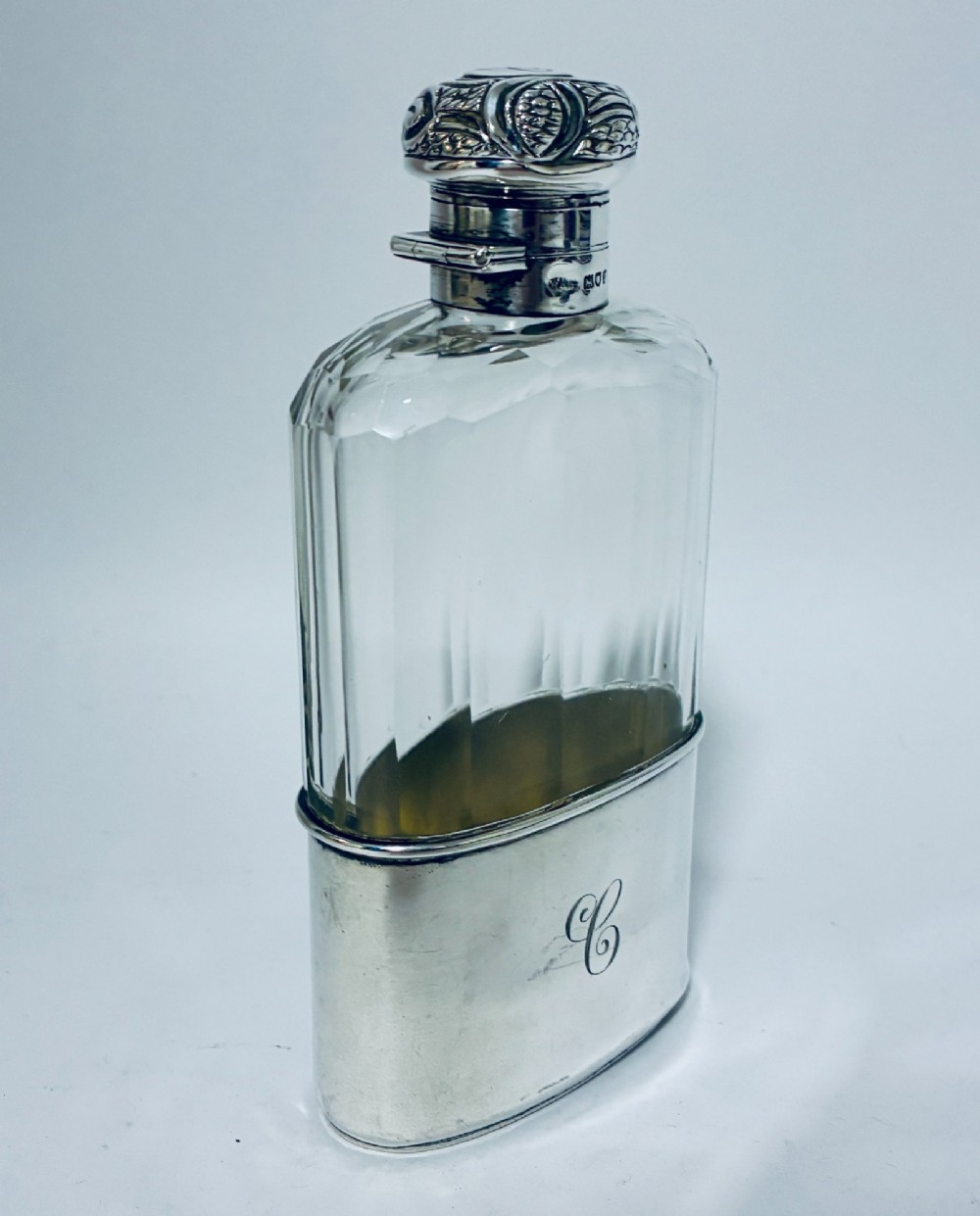 An antique cut-glass hip flask featuring a hallmarked sterling silver collar, chased cap, and a removable silver base cup engraved with the letter C. View V