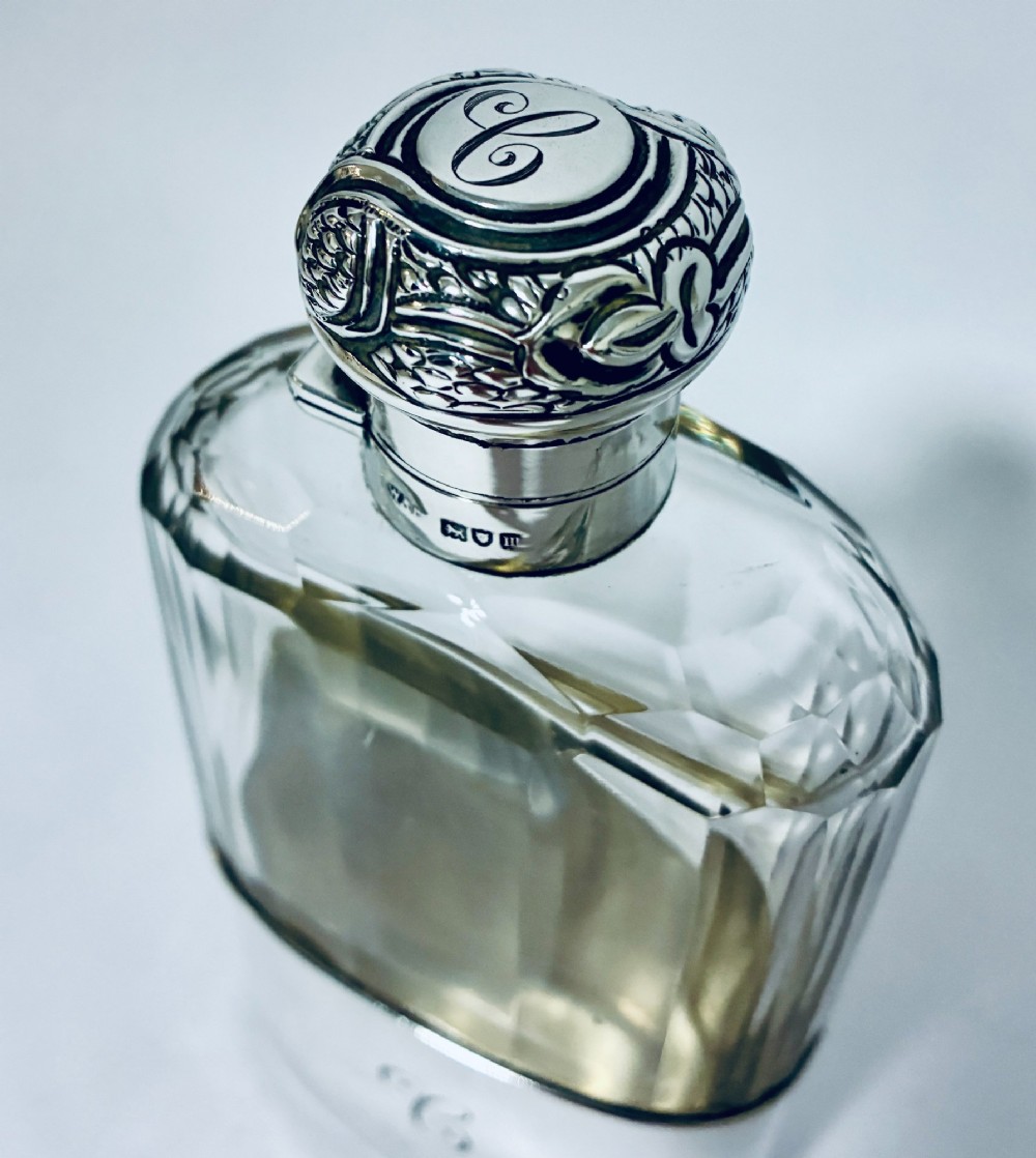An antique cut-glass hip flask featuring a hallmarked sterling silver collar, chased cap, and a removable silver base cup engraved with the letter C. View VII