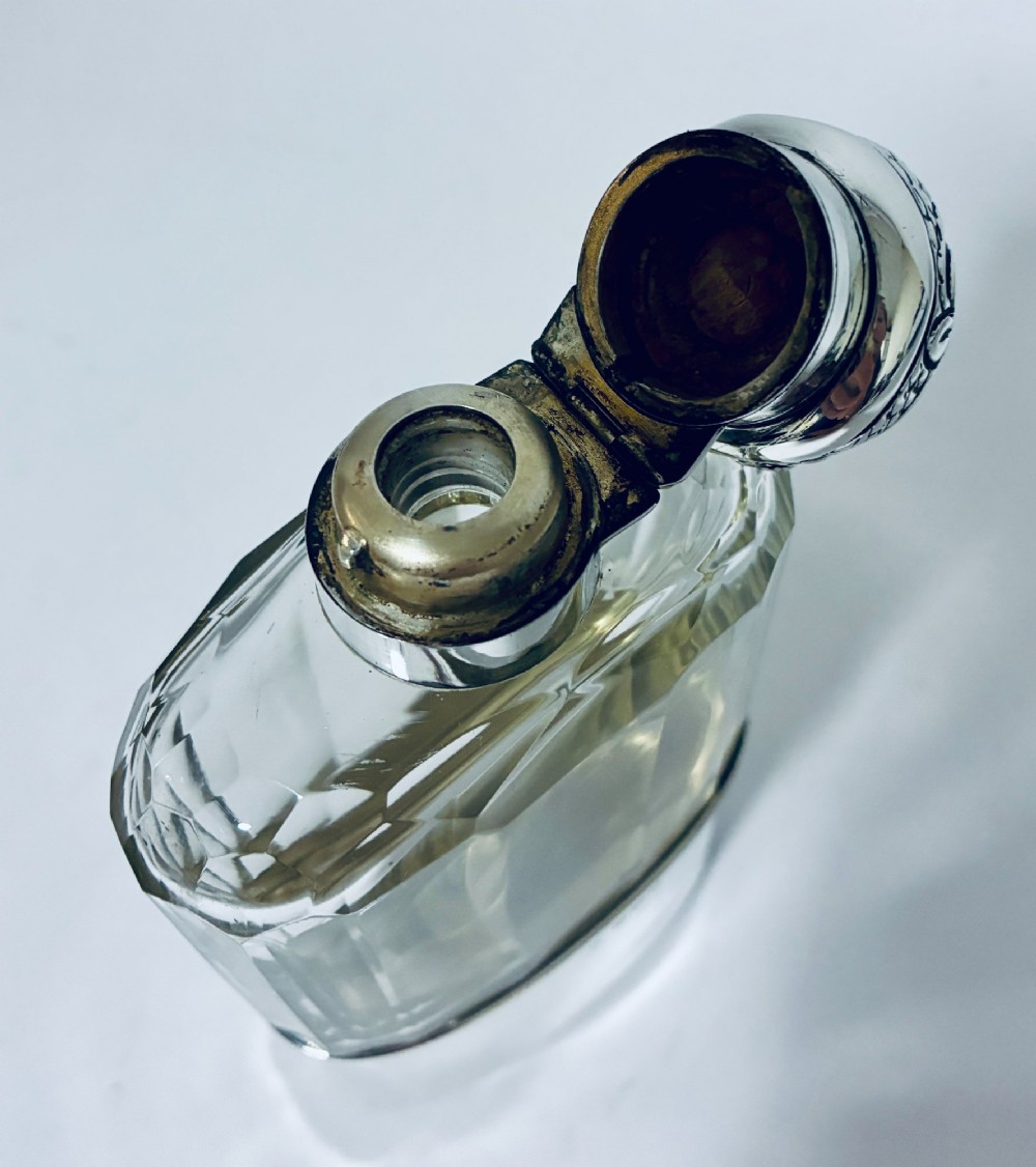 An antique cut-glass hip flask featuring a hallmarked sterling silver collar, chased cap, and a removable silver base cup engraved with the letter C. View X