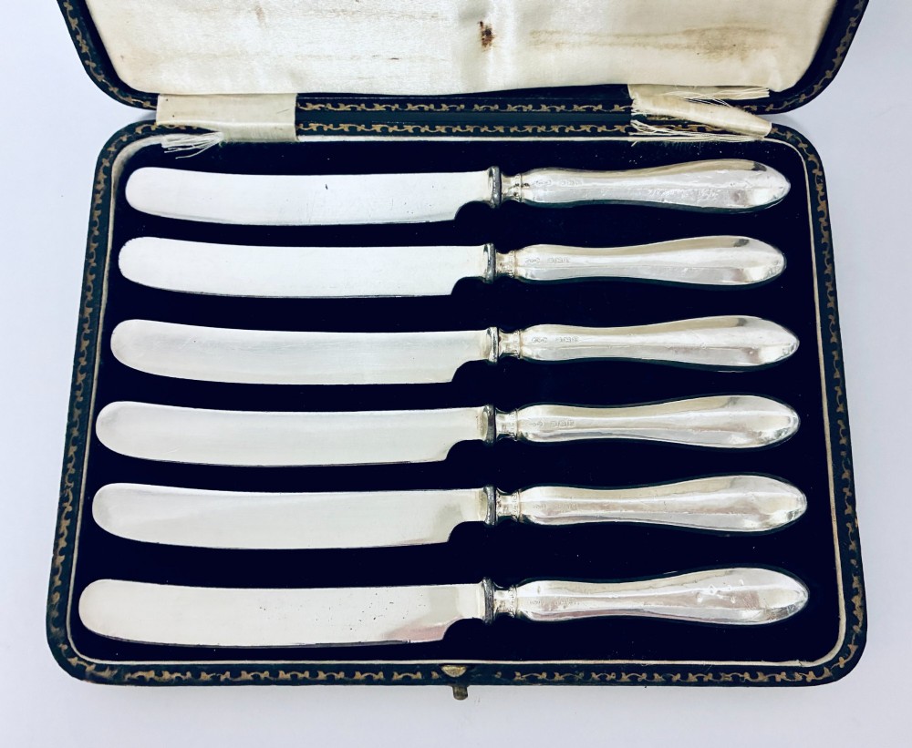 A set of six silver-handled butter knives presented in an open velvet- and silk-lined storage case. View II