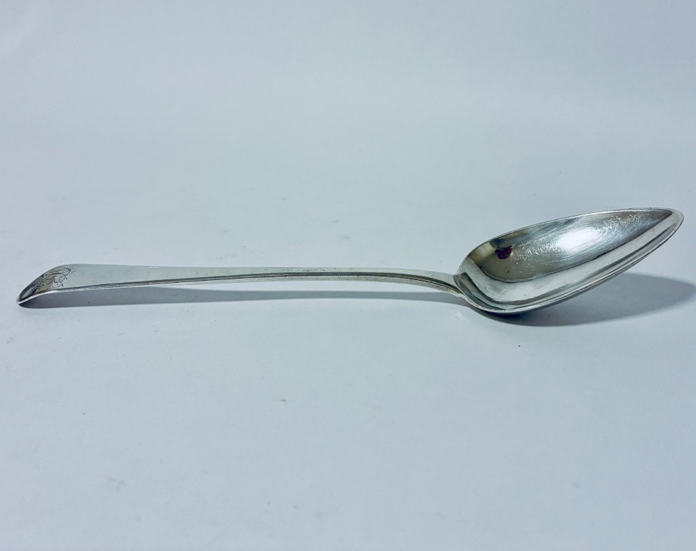 A Georgian sterling silver serving spoon featuring an Old English pattern stem with an engraved crest and a tapered oval bowl against a white backdrop. View II