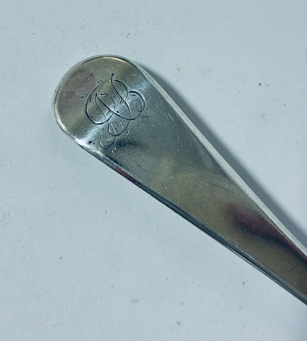 A Georgian sterling silver serving spoon featuring an Old English pattern stem with an engraved crest and a tapered oval bowl against a white backdrop. View III