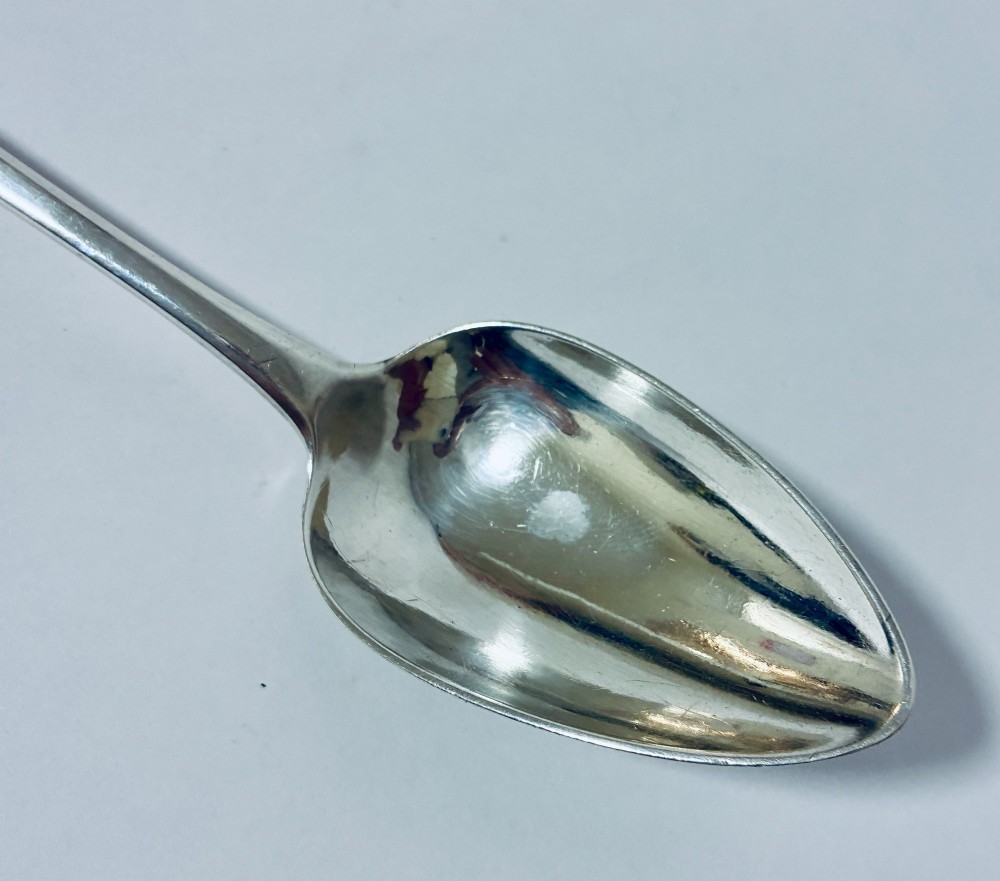 A Georgian sterling silver serving spoon featuring an Old English pattern stem with an engraved crest and a tapered oval bowl against a white backdrop. View IV