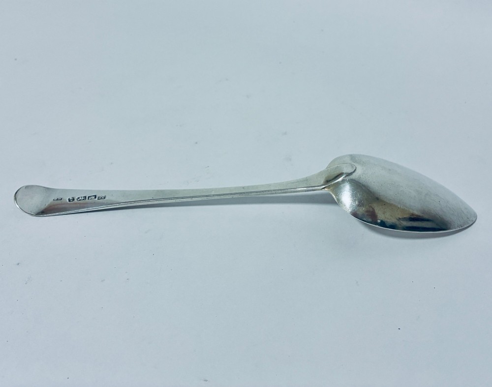 A Georgian sterling silver serving spoon featuring an Old English pattern stem with an engraved crest and a tapered oval bowl against a white backdrop. View V