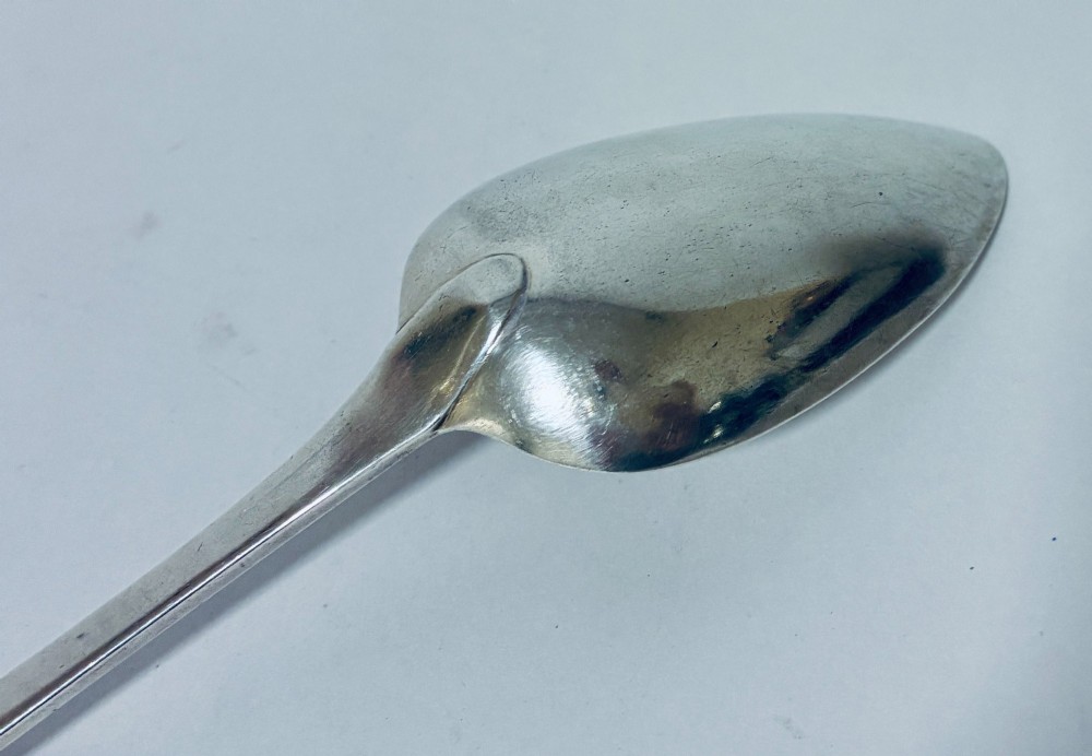 A Georgian sterling silver serving spoon featuring an Old English pattern stem with an engraved crest and a tapered oval bowl against a white backdrop. View VI