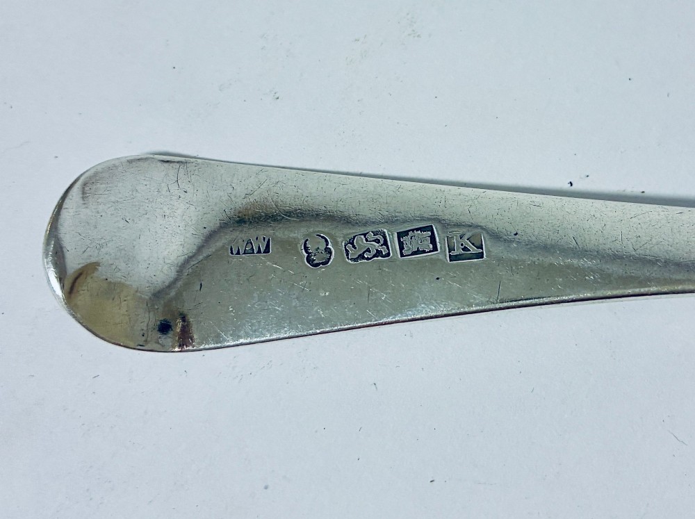 A Georgian sterling silver serving spoon featuring an Old English pattern stem with an engraved crest and a tapered oval bowl against a white backdrop. View VII