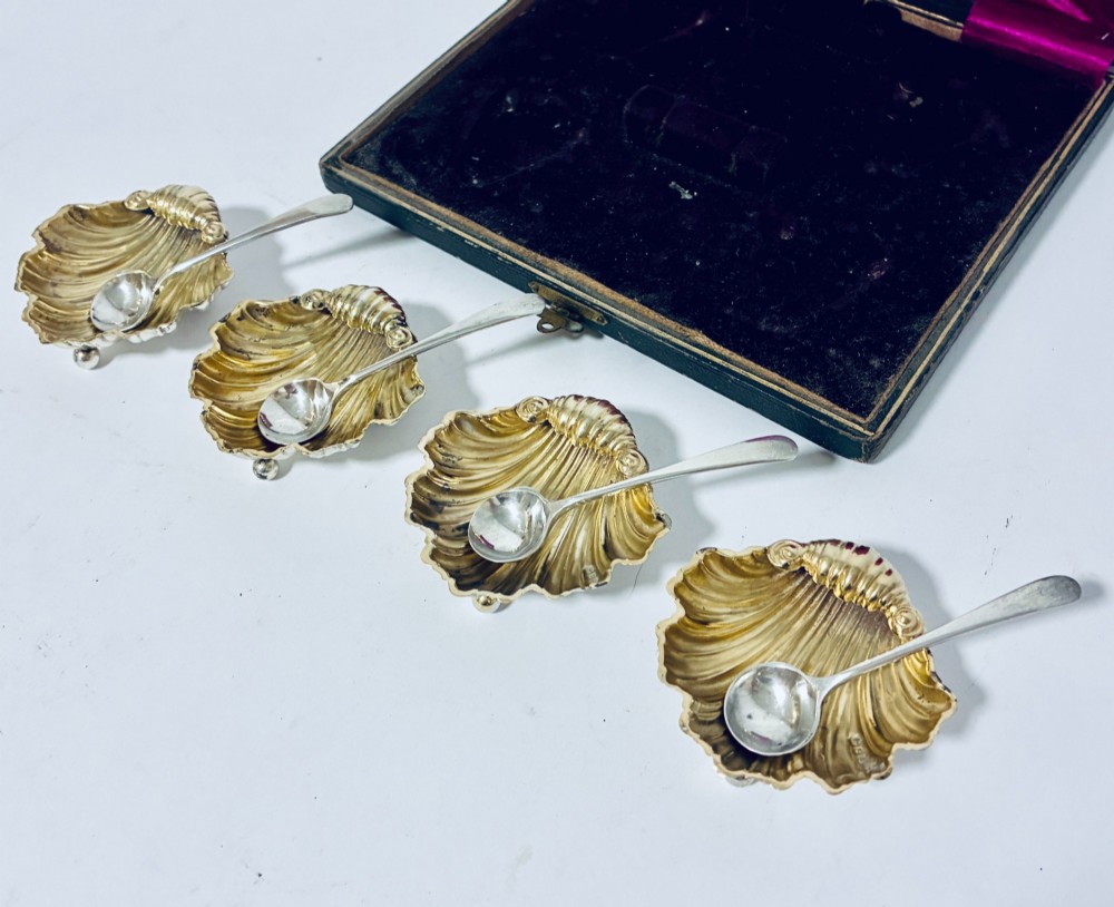 A cased set of four Victorian shell-shaped silver salt cellars with gilded interiors and two matching silver spoons in a velvet-lined box. View V