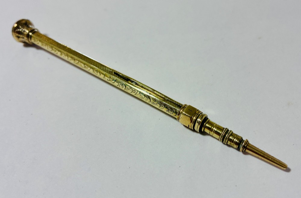 An antique gold propelling pencil featuring detailed scroll engraving along its slender hexagonal barrel and a polished tip. View II