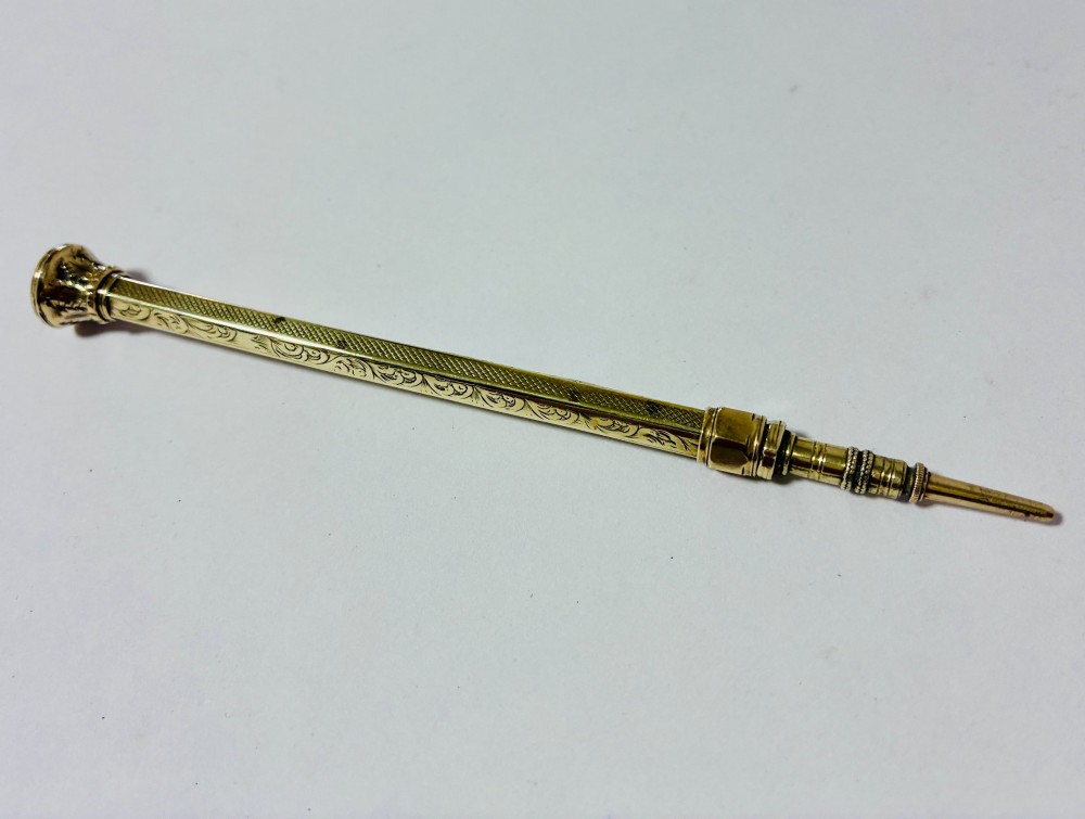 An antique gold propelling pencil featuring detailed scroll engraving along its slender hexagonal barrel and a polished tip. View III