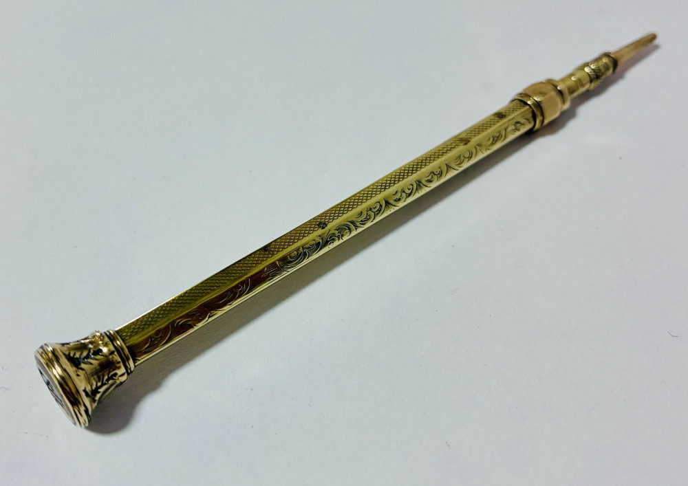 An antique gold propelling pencil featuring detailed scroll engraving along its slender hexagonal barrel and a polished tip. View IV