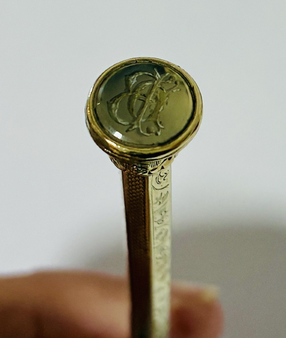An antique gold propelling pencil featuring detailed scroll engraving along its slender hexagonal barrel and a polished tip. View V