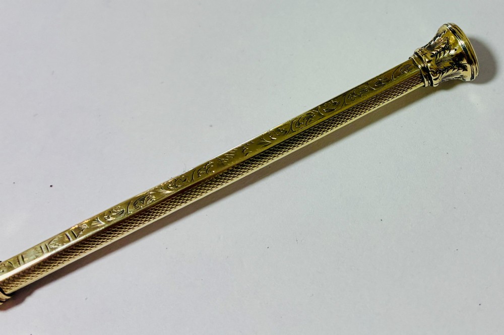 An antique gold propelling pencil featuring detailed scroll engraving along its slender hexagonal barrel and a polished tip. View VII