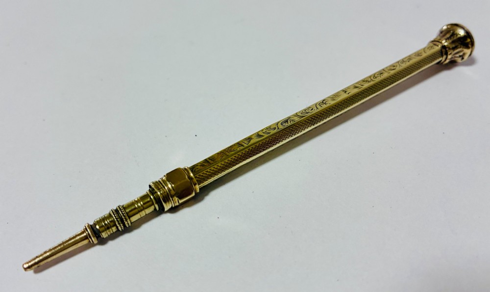 An antique gold propelling pencil featuring detailed scroll engraving along its slender hexagonal barrel and a polished tip. View VIII