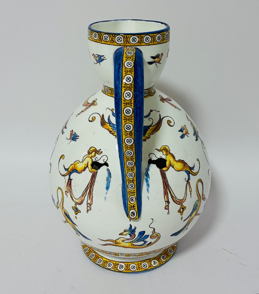 A white tin-glazed earthenware ewer decorated with hand-painted Renaissance grotesque figures, a central crest, and a blue handle. View V