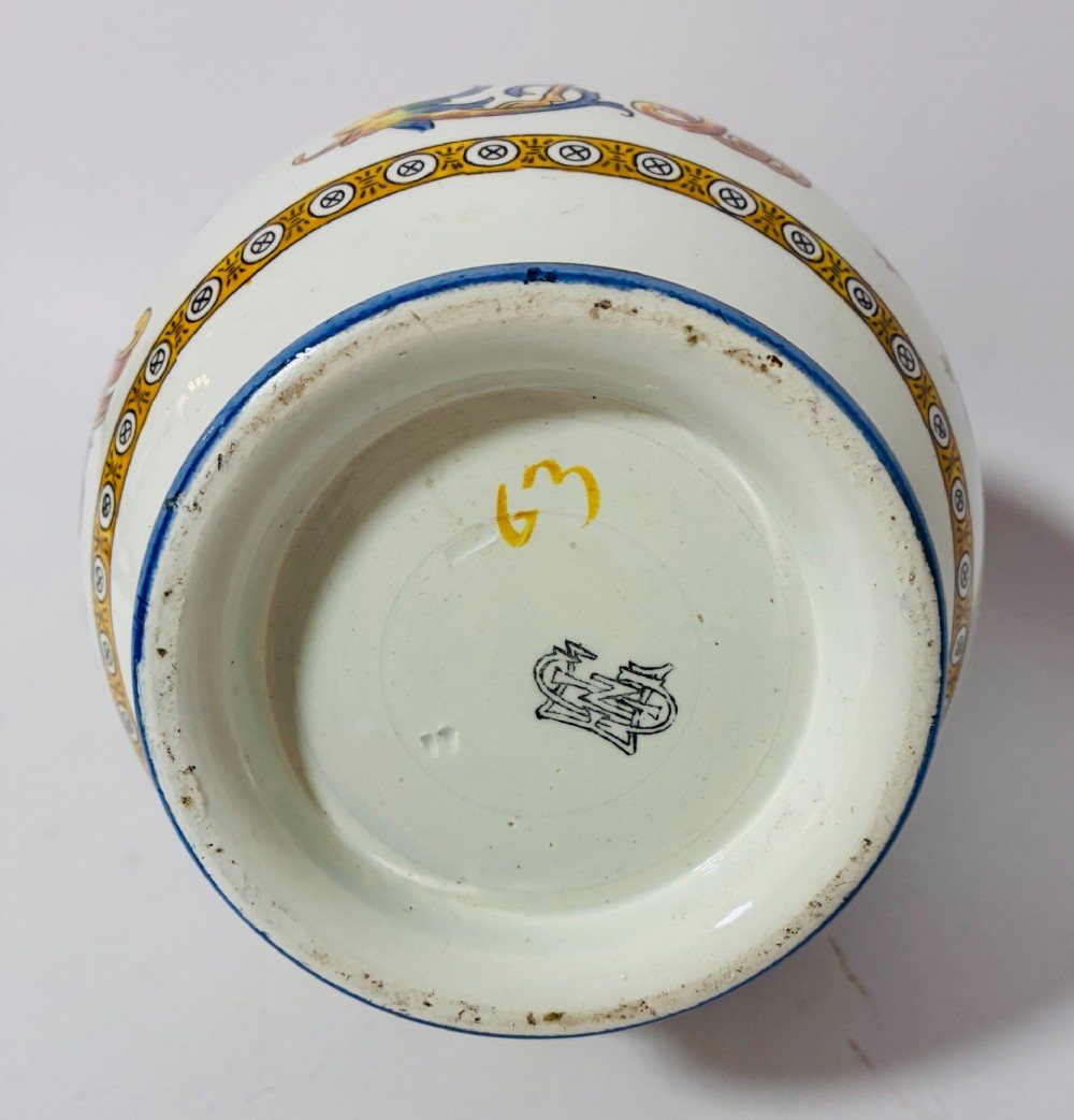 A white tin-glazed earthenware ewer decorated with hand-painted Renaissance grotesque figures, a central crest, and a blue handle. View X