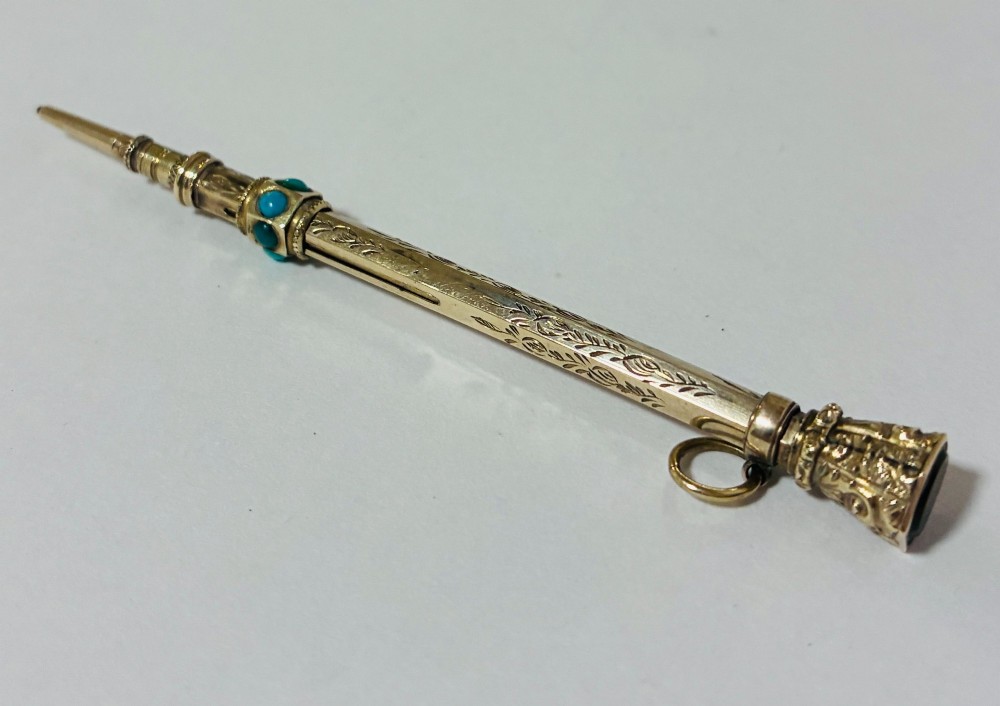 An ornate Victorian gold propelling pencil featuring engraved floral motifs, set with round turquoise cabochons and fitted with a suspension ring. View II
