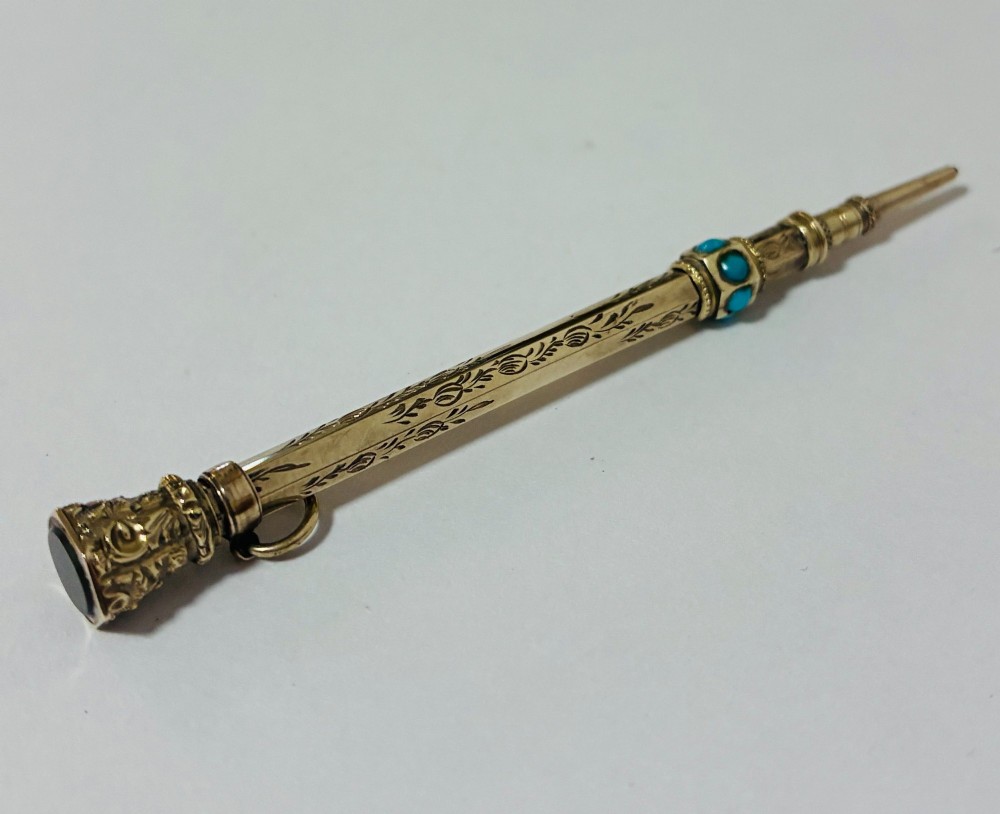 An ornate Victorian gold propelling pencil featuring engraved floral motifs, set with round turquoise cabochons and fitted with a suspension ring. View III