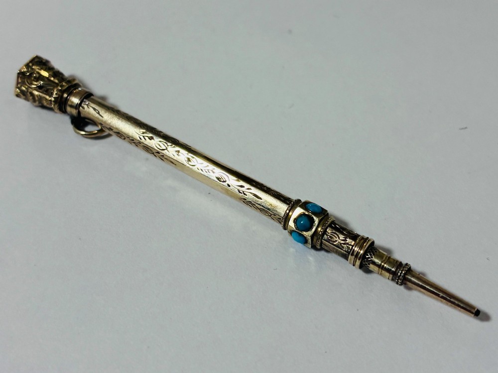 An ornate Victorian gold propelling pencil featuring engraved floral motifs, set with round turquoise cabochons and fitted with a suspension ring. View V
