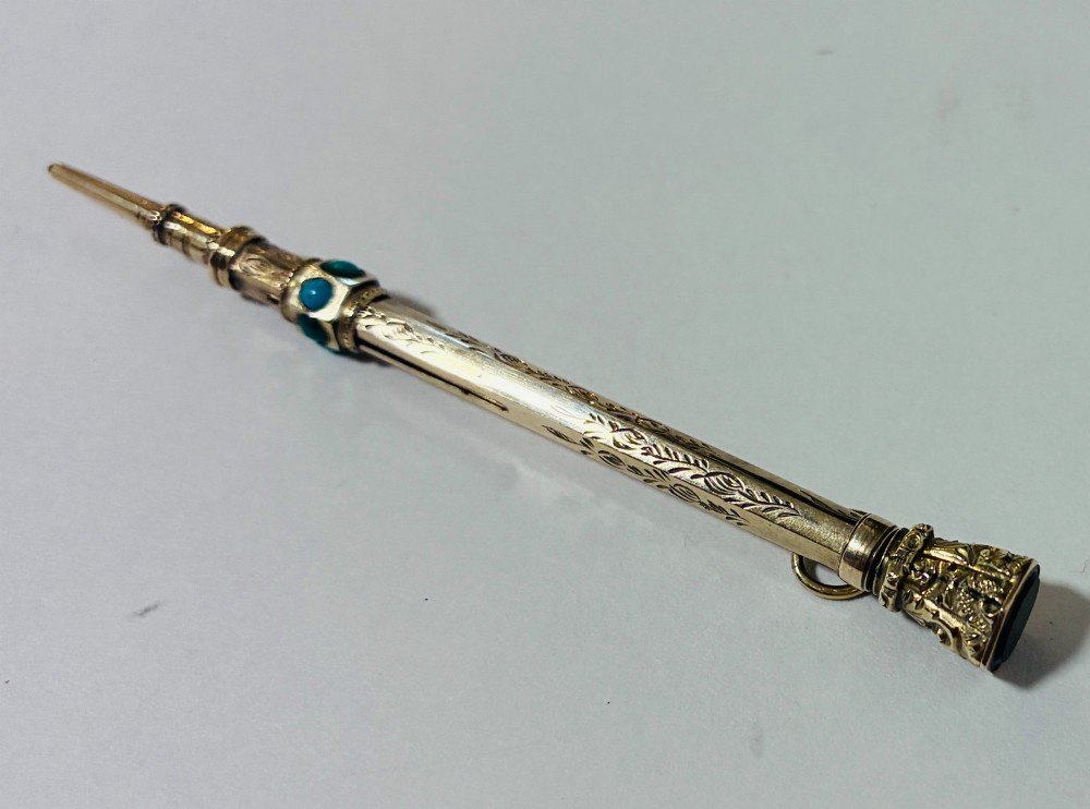 An ornate Victorian gold propelling pencil featuring engraved floral motifs, set with round turquoise cabochons and fitted with a suspension ring. View VI