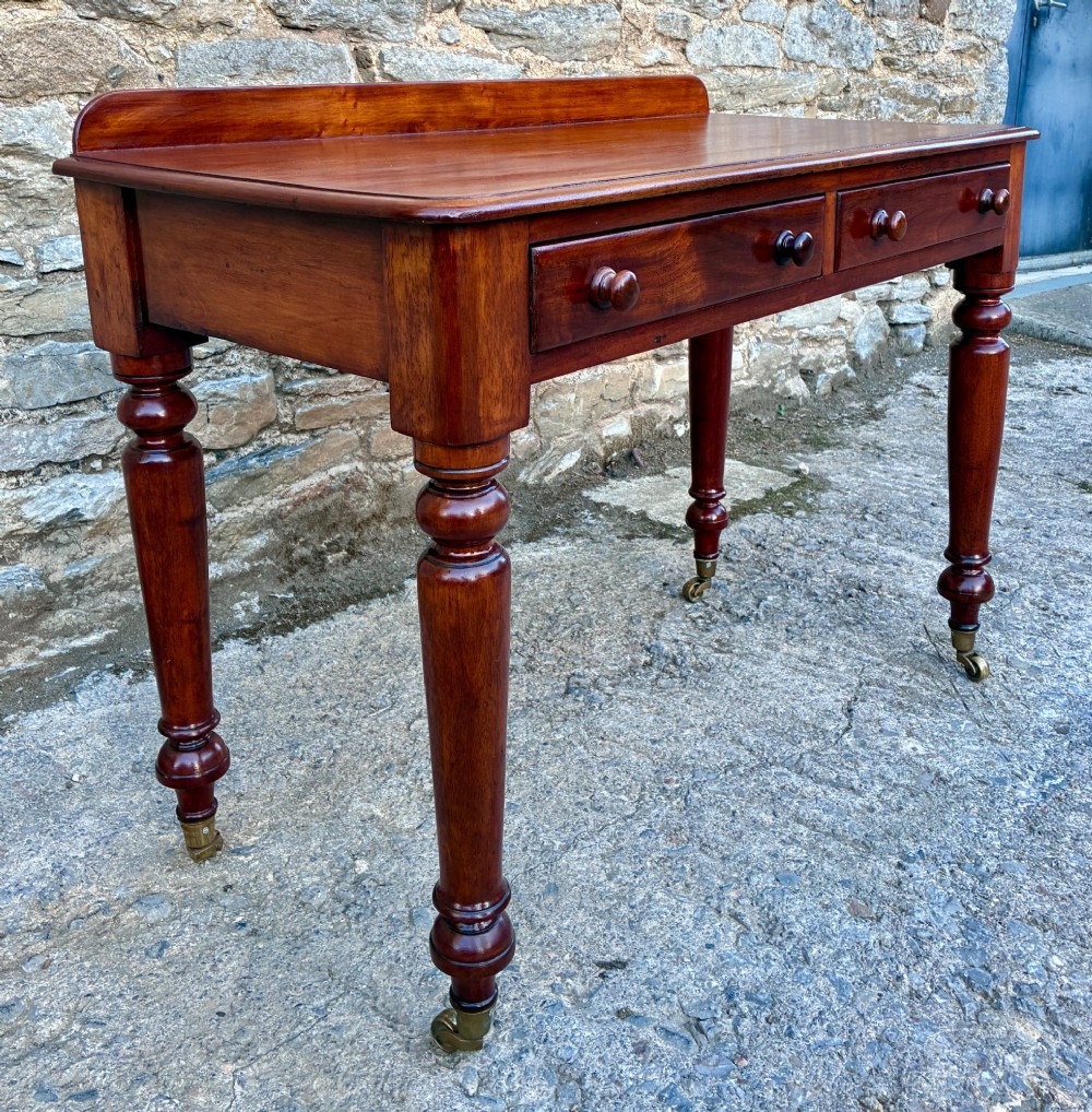 A Victorian mahogany side table featuring a low rear gallery, two drawers with wooden knob handles, turned legs, and brass castors. View III