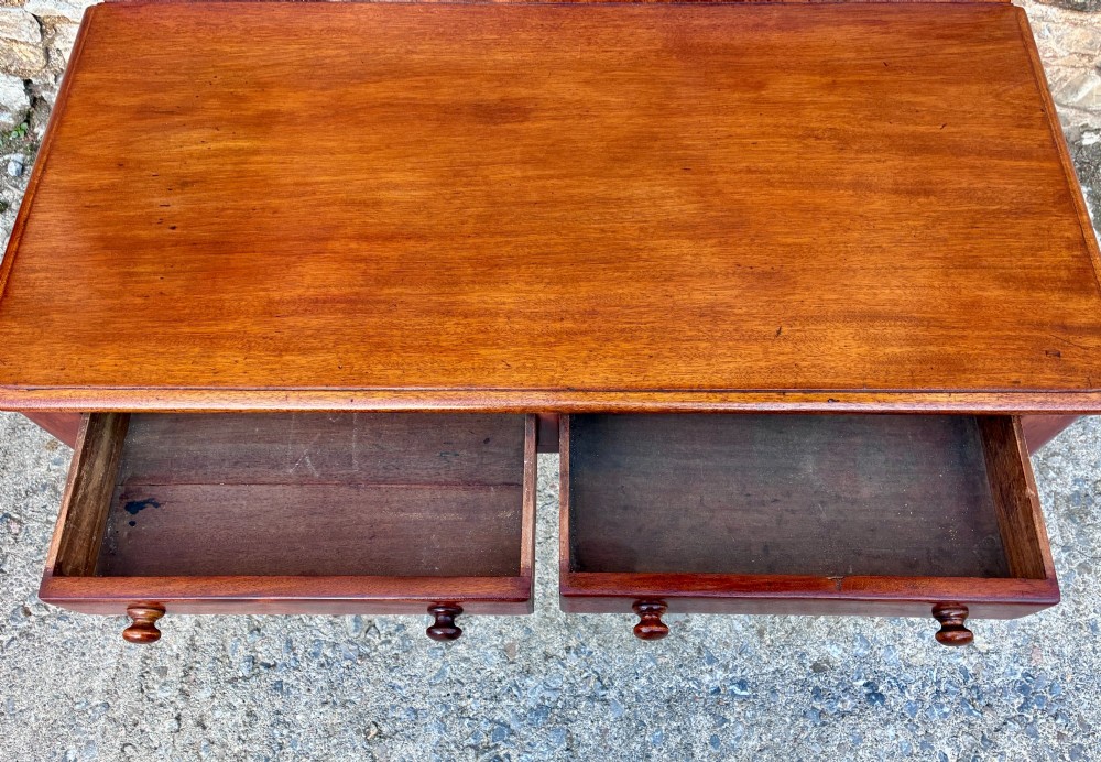 A Victorian mahogany side table featuring a low rear gallery, two drawers with wooden knob handles, turned legs, and brass castors. View V