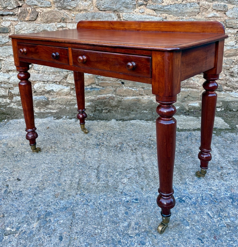 A Victorian mahogany side table featuring a low rear gallery, two drawers with wooden knob handles, turned legs, and brass castors. View VII