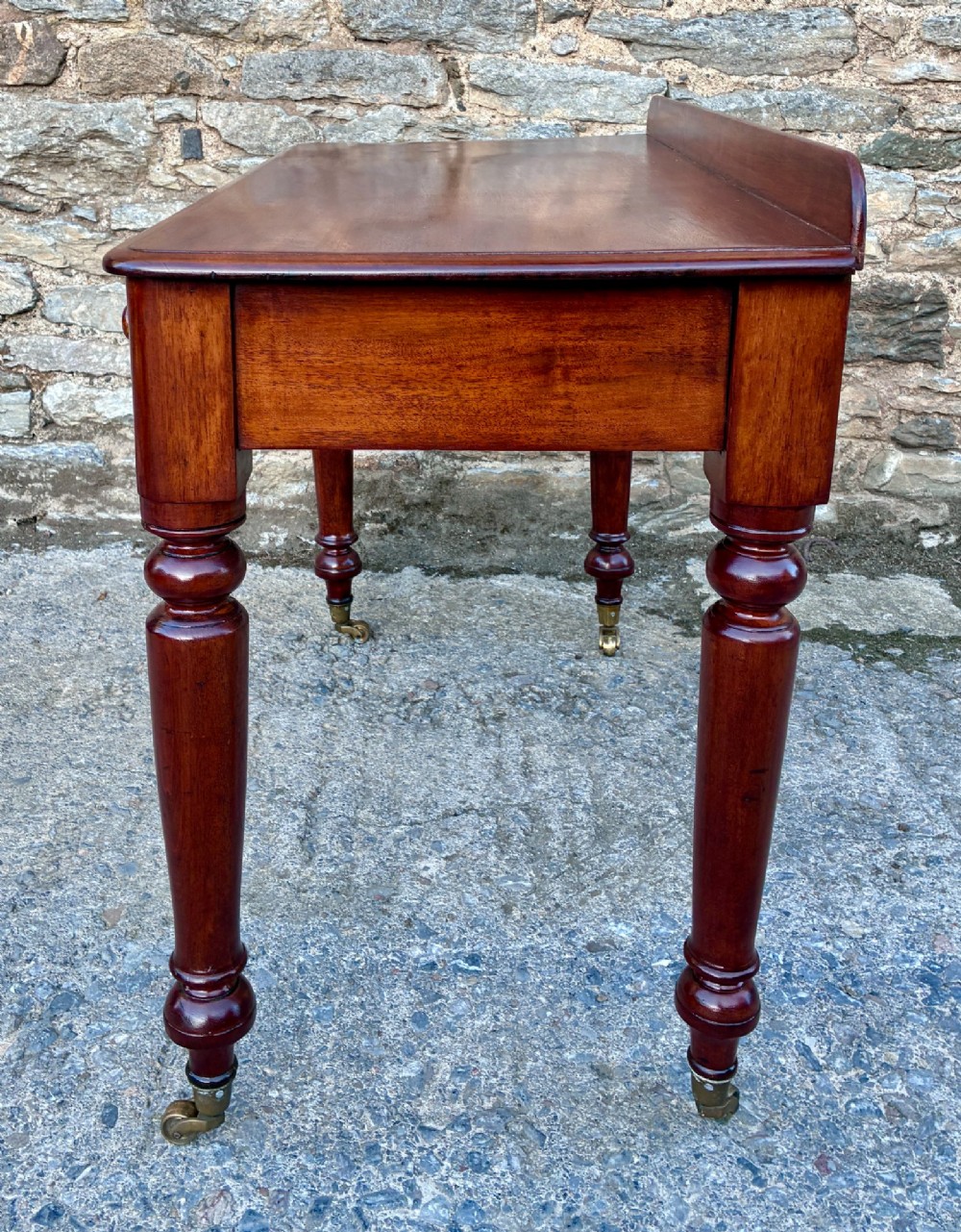 A Victorian mahogany side table featuring a low rear gallery, two drawers with wooden knob handles, turned legs, and brass castors. View VIII