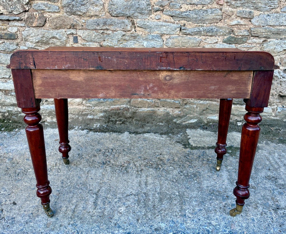 A Victorian mahogany side table featuring a low rear gallery, two drawers with wooden knob handles, turned legs, and brass castors. View IX