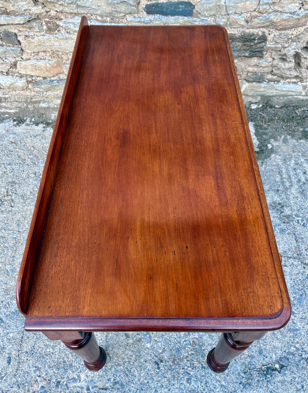 A Victorian mahogany side table featuring a low rear gallery, two drawers with wooden knob handles, turned legs, and brass castors. View XI