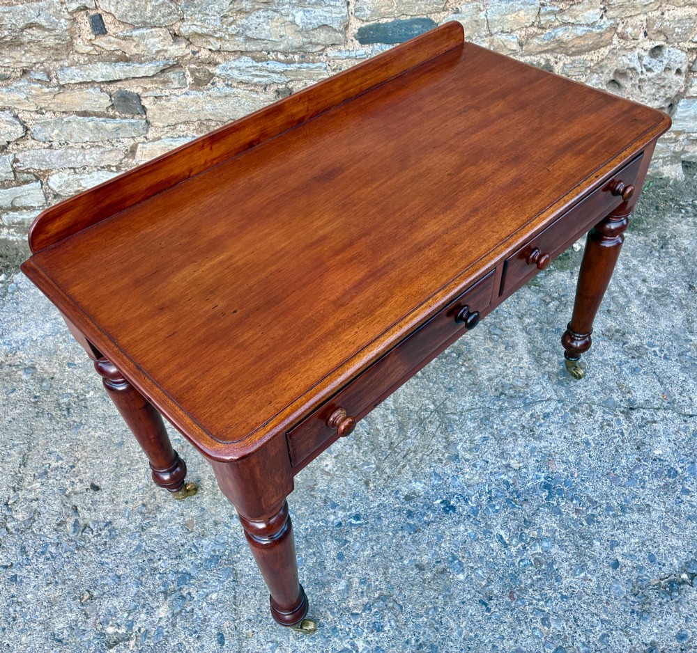 A Victorian mahogany side table featuring a low rear gallery, two drawers with wooden knob handles, turned legs, and brass castors. View XII