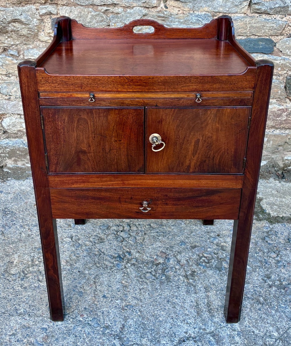 A Georgian mahogany tray top commode featuring a gallery top with pierced carrying handles, double cupboard doors, and a lower drawer on square legs.