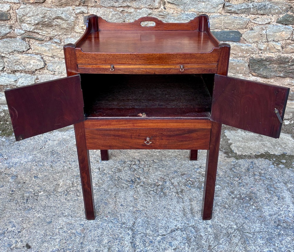 A Georgian mahogany tray top commode featuring a gallery top with pierced carrying handles, double cupboard doors, and a lower drawer on square legs. View V