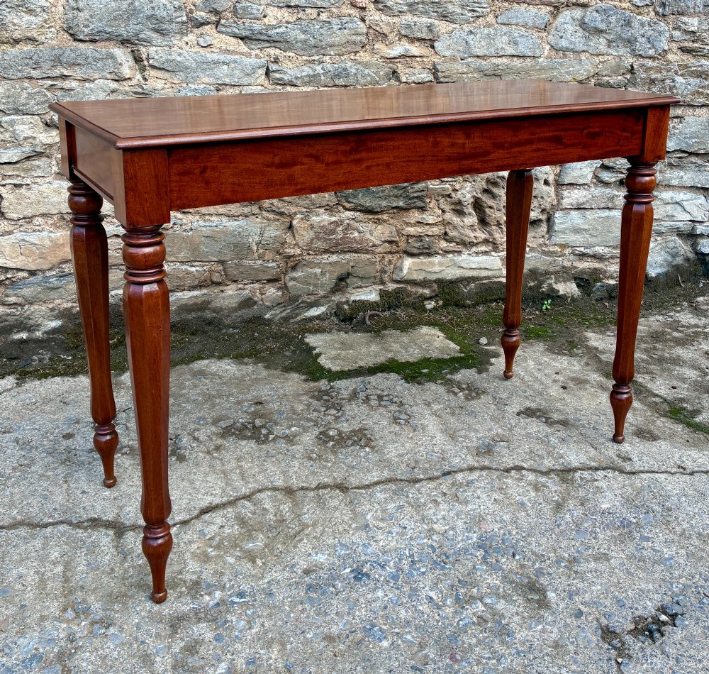 A rectangular Victorian mahogany console table featuring a smooth polished top surface, straight apron, and four turned legs. View VII