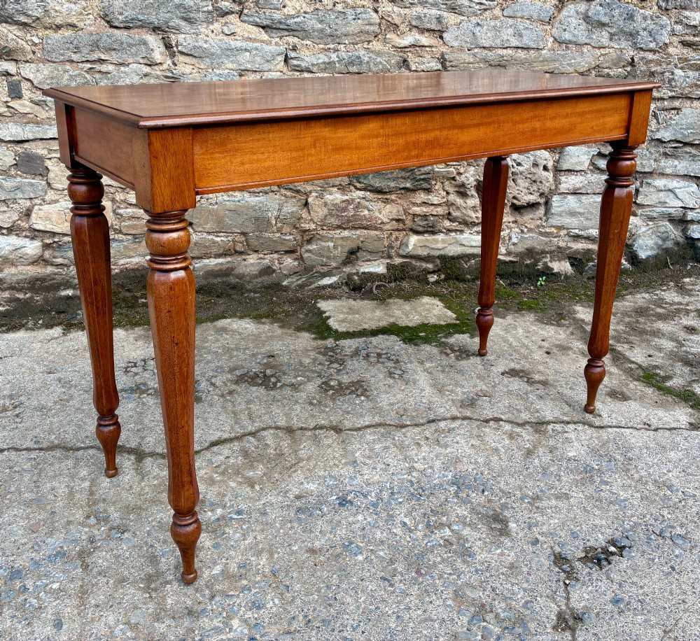 A rectangular Victorian mahogany console table featuring a smooth polished top surface, straight apron, and four turned legs. View IX