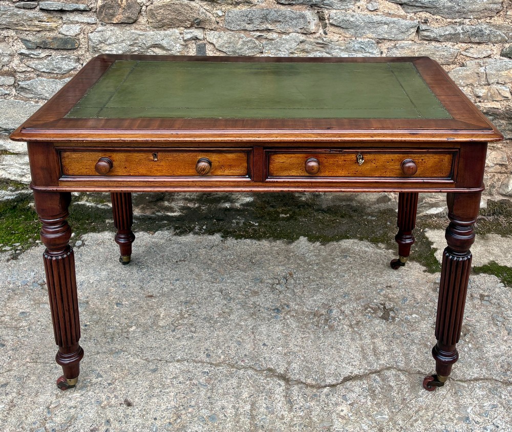 A Victorian mahogany writing table featuring a green leather top, two front drawers with turned wooden knobs, and fluted turned legs on brass castors.