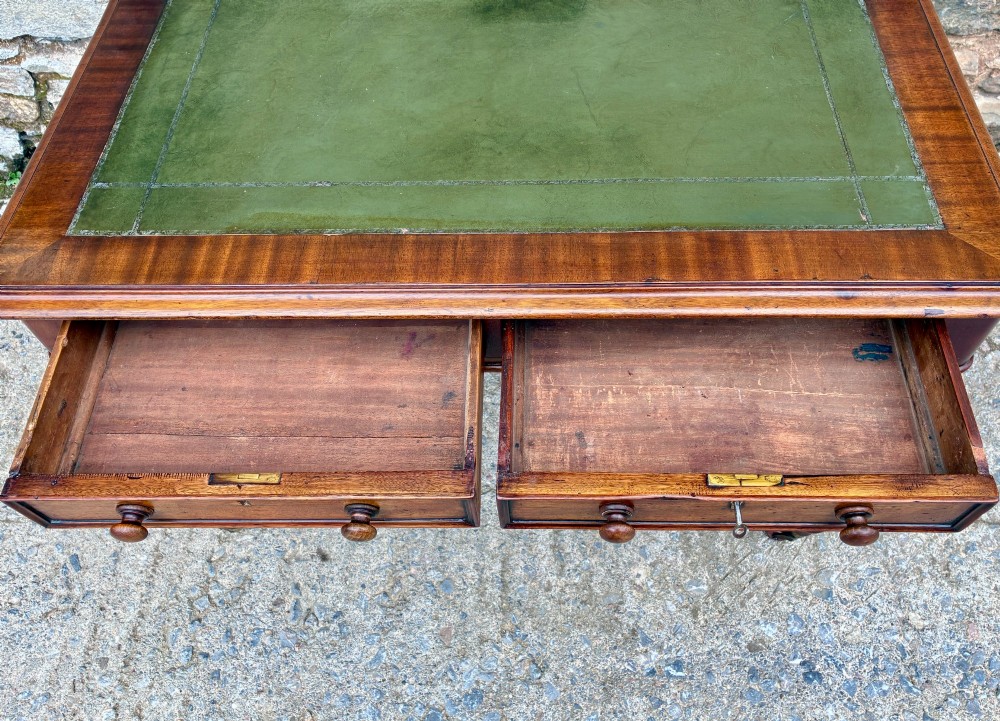 A Victorian mahogany writing table featuring a green leather top, two front drawers with turned wooden knobs, and fluted turned legs on brass castors. View VII