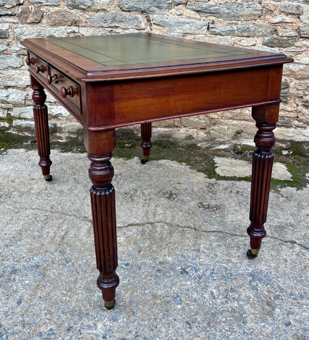 A Victorian mahogany writing table featuring a green leather top, two front drawers with turned wooden knobs, and fluted turned legs on brass castors. View XI