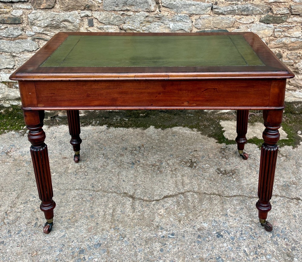 A Victorian mahogany writing table featuring a green leather top, two front drawers with turned wooden knobs, and fluted turned legs on brass castors. View XIII