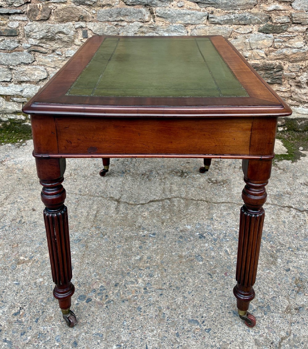 A Victorian mahogany writing table featuring a green leather top, two front drawers with turned wooden knobs, and fluted turned legs on brass castors. View XIV