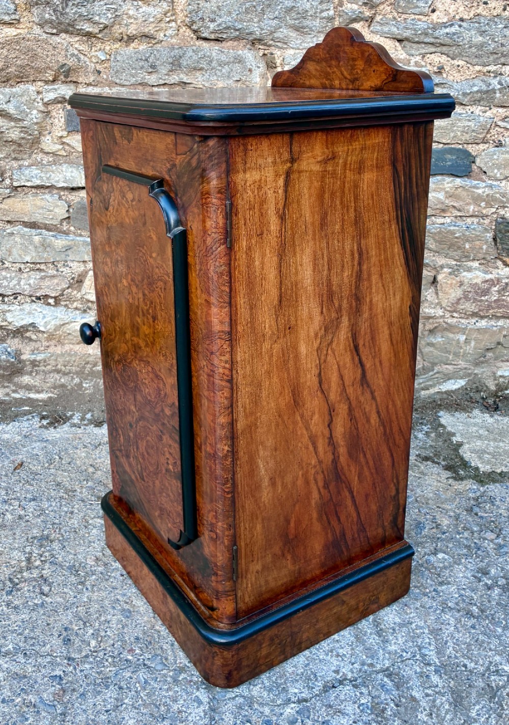 A Victorian burr walnut pot cupboard featuring a single door with ebonised moulding, a rounded top edge, shaped splashback gallery, and dark wooden knob. View VI
