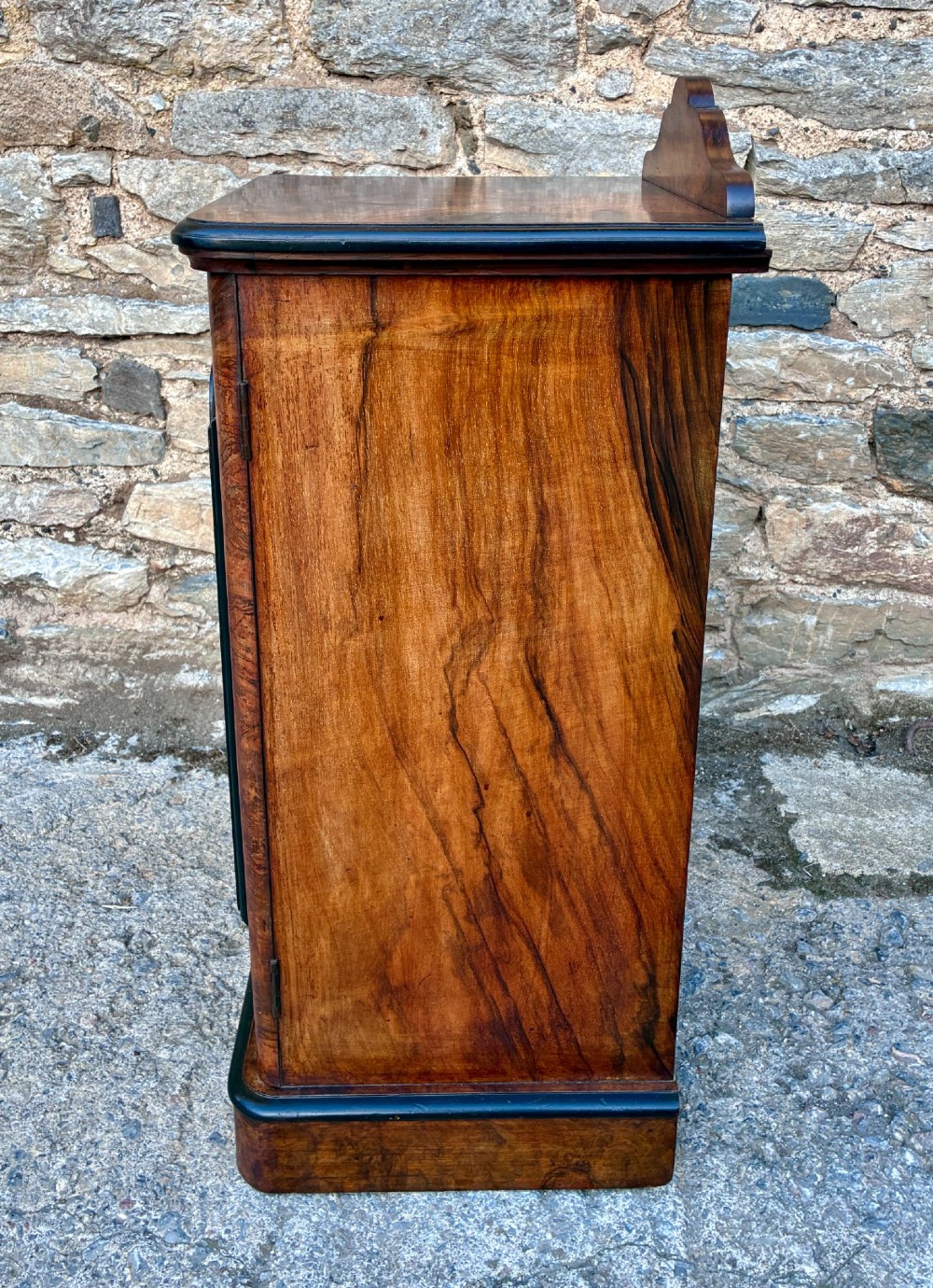 A Victorian burr walnut pot cupboard featuring a single door with ebonised moulding, a rounded top edge, shaped splashback gallery, and dark wooden knob. View VII