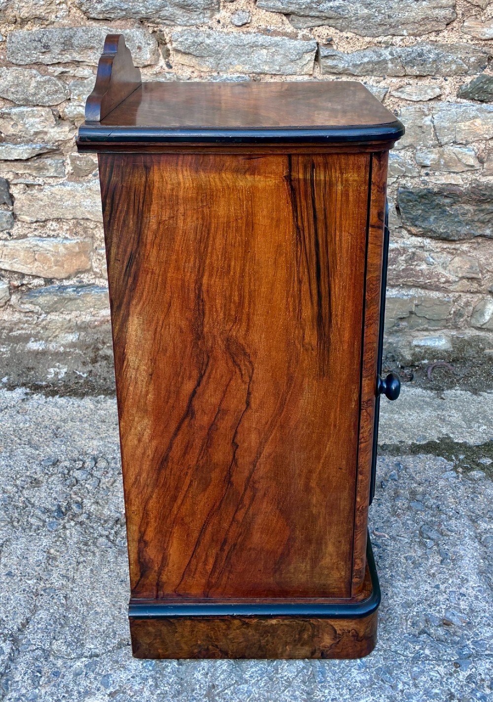 A Victorian burr walnut pot cupboard featuring a single door with ebonised moulding, a rounded top edge, shaped splashback gallery, and dark wooden knob. View IX