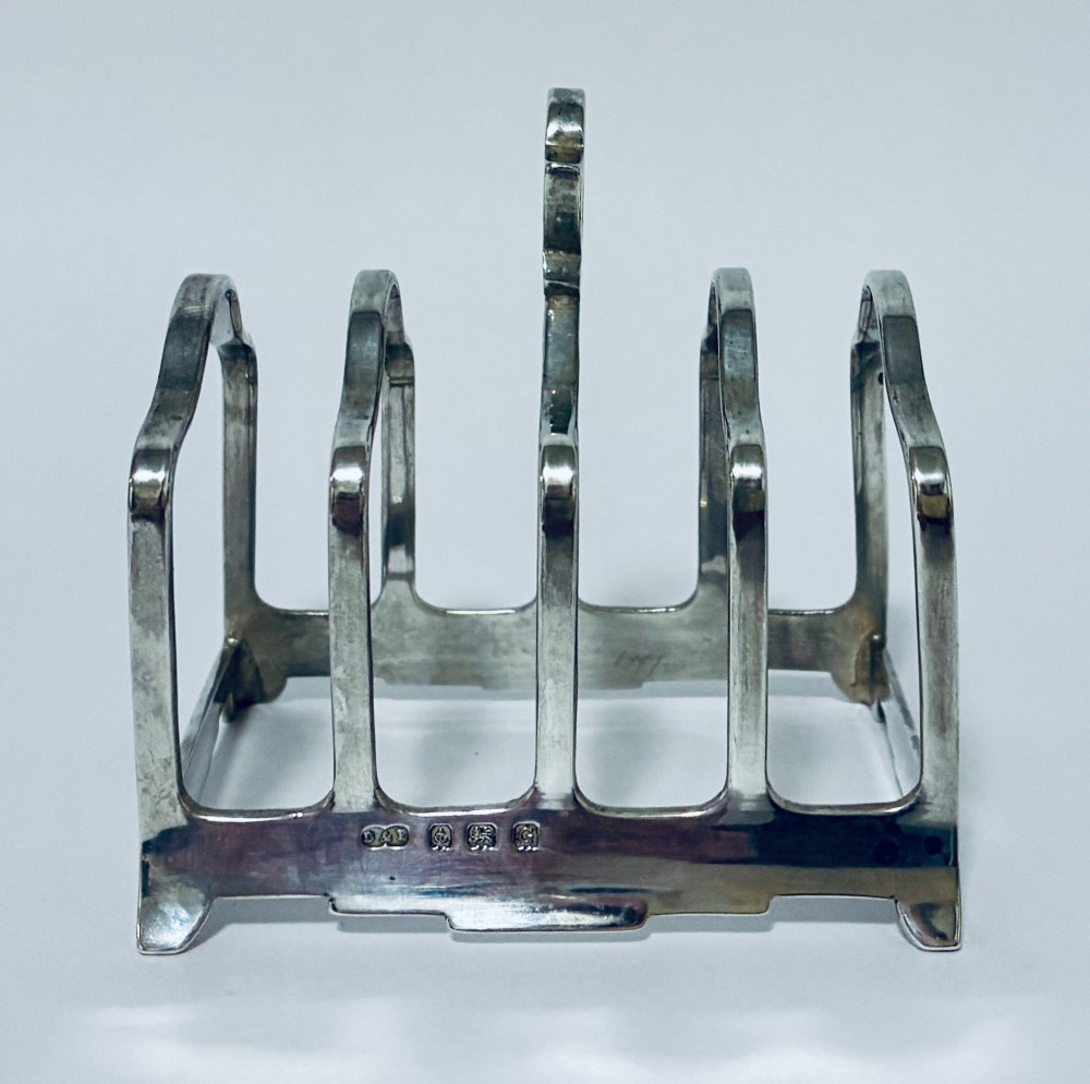 A Victorian sterling silver toast rack featuring four arched dividers, a central loop handle, and stamped hallmarks along the front base rail.