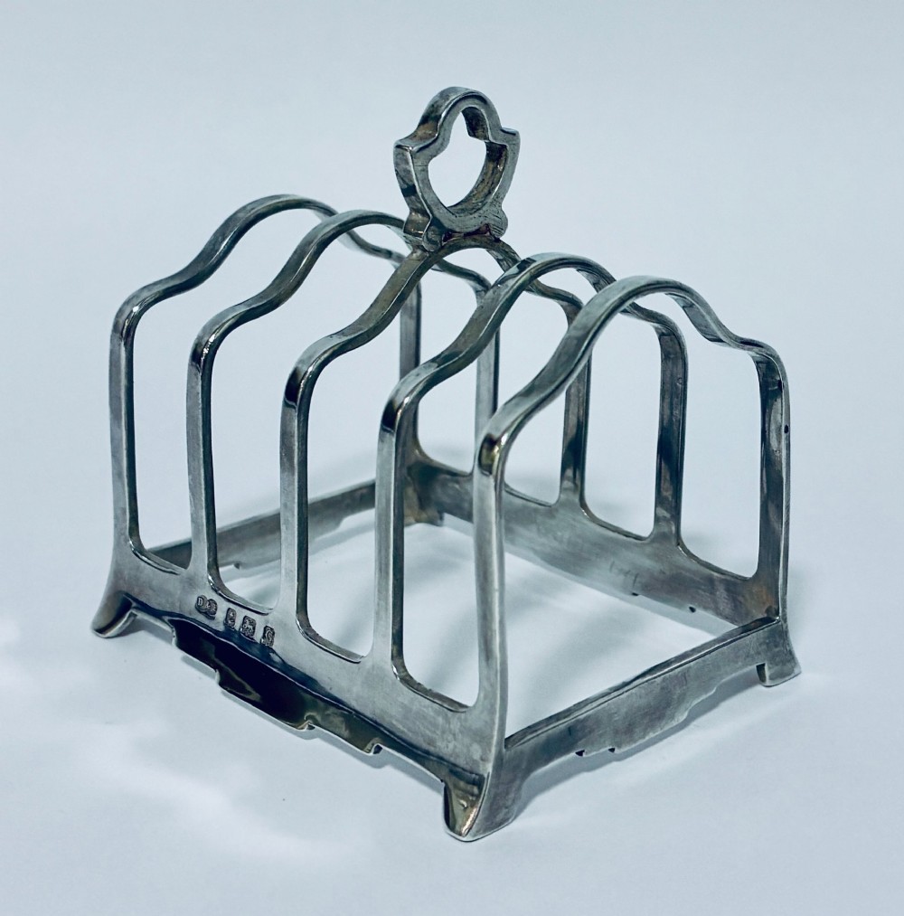 A Victorian sterling silver toast rack featuring four arched dividers, a central loop handle, and stamped hallmarks along the front base rail. View II