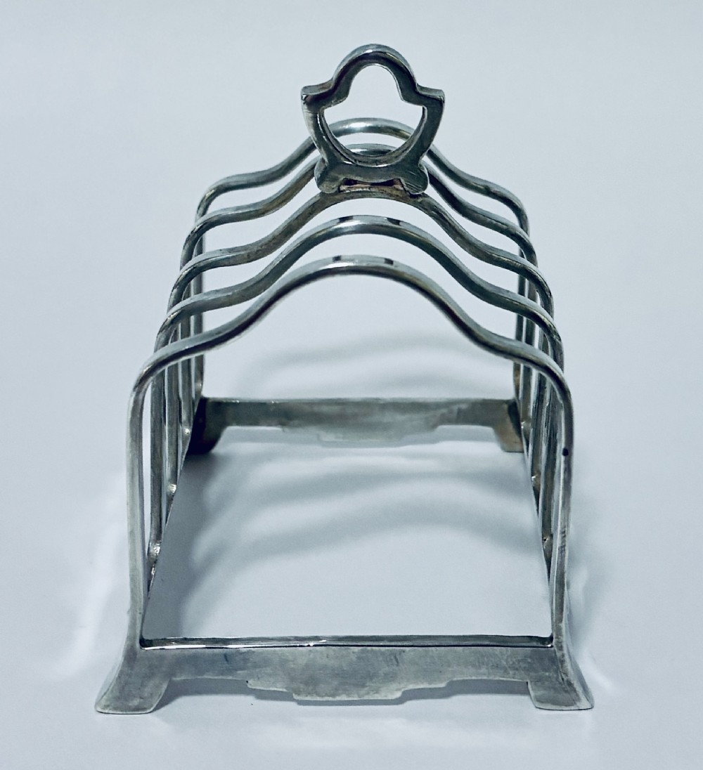 A Victorian sterling silver toast rack featuring four arched dividers, a central loop handle, and stamped hallmarks along the front base rail. View III