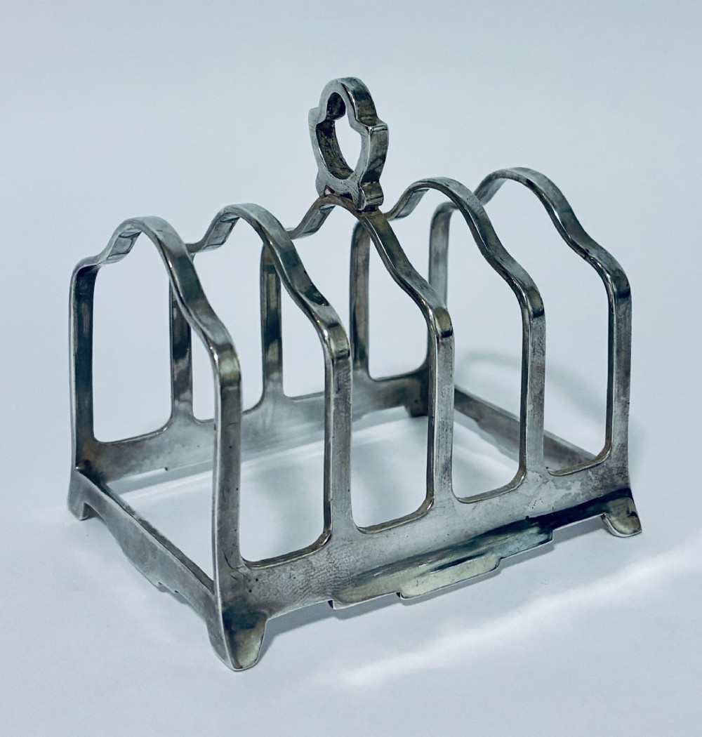 A Victorian sterling silver toast rack featuring four arched dividers, a central loop handle, and stamped hallmarks along the front base rail. View IV